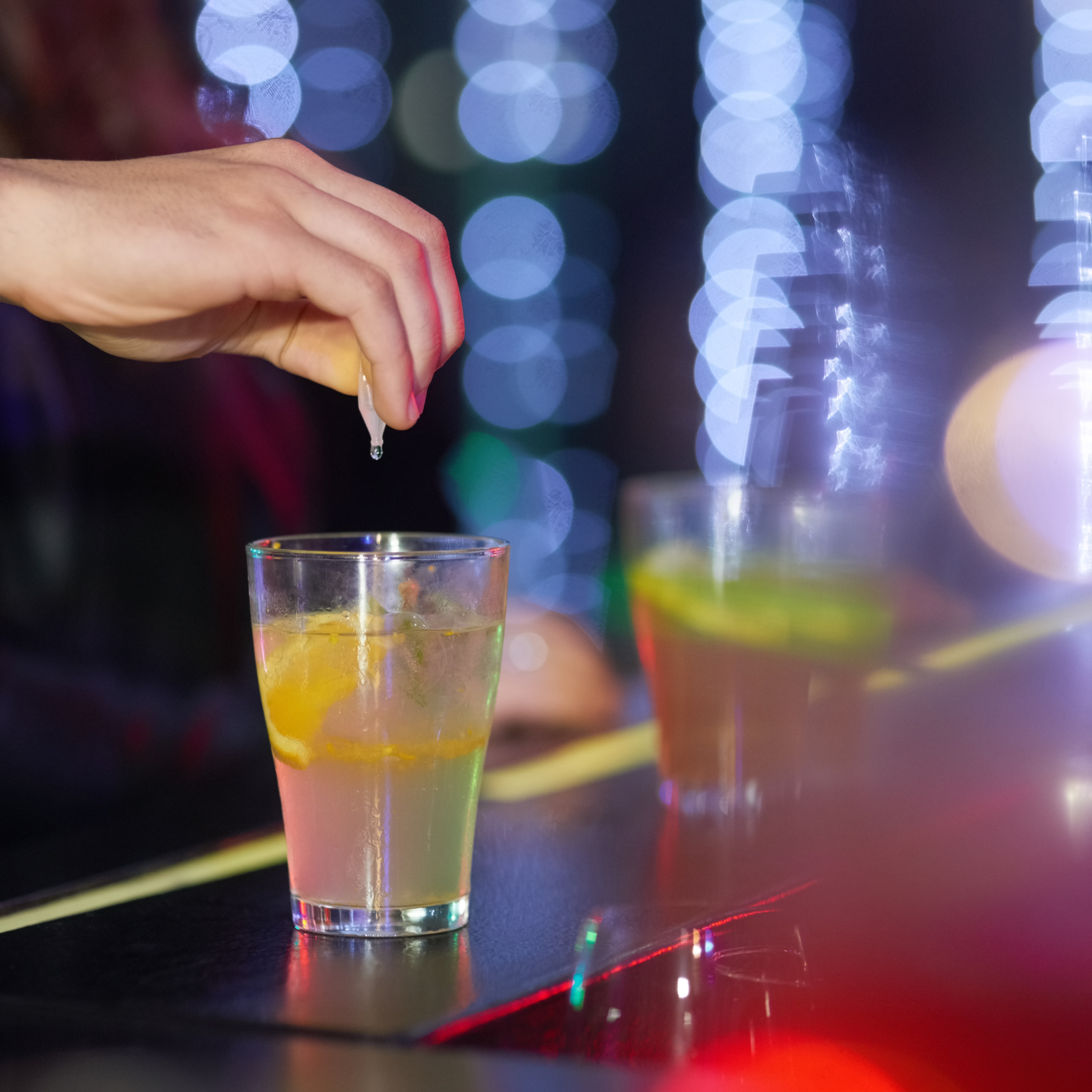 Closeup of a hand dropping an unknown substance into an alcoholic drink at a bar.