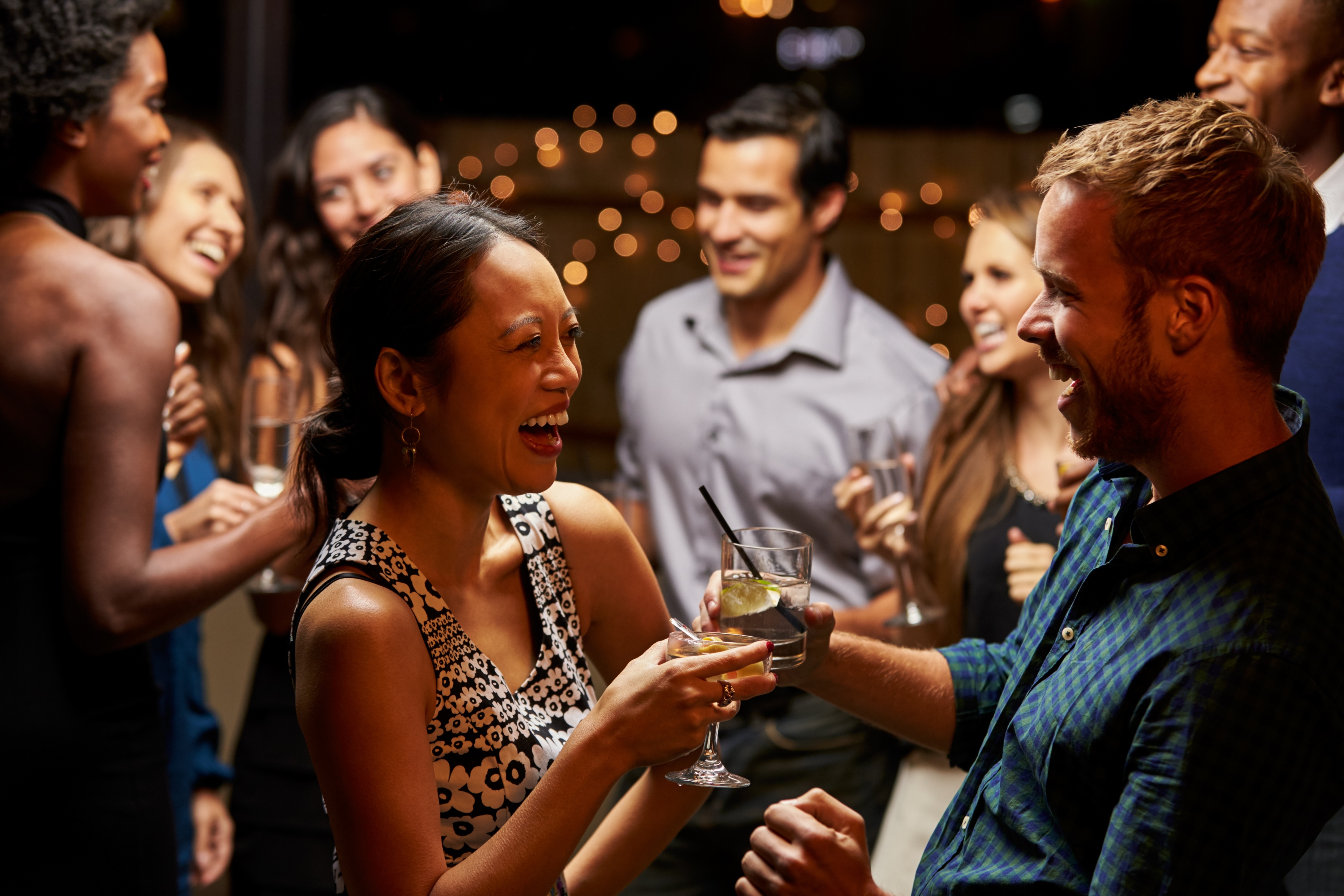 A young man and woman clink their alcoholic beverages together at a party and show signs of alcohol consumption.