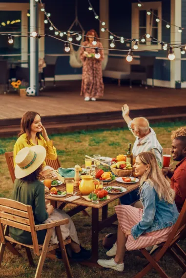 Group of mixed age family members sitting at a table outdoors with food and drinks and smiles on their faces.