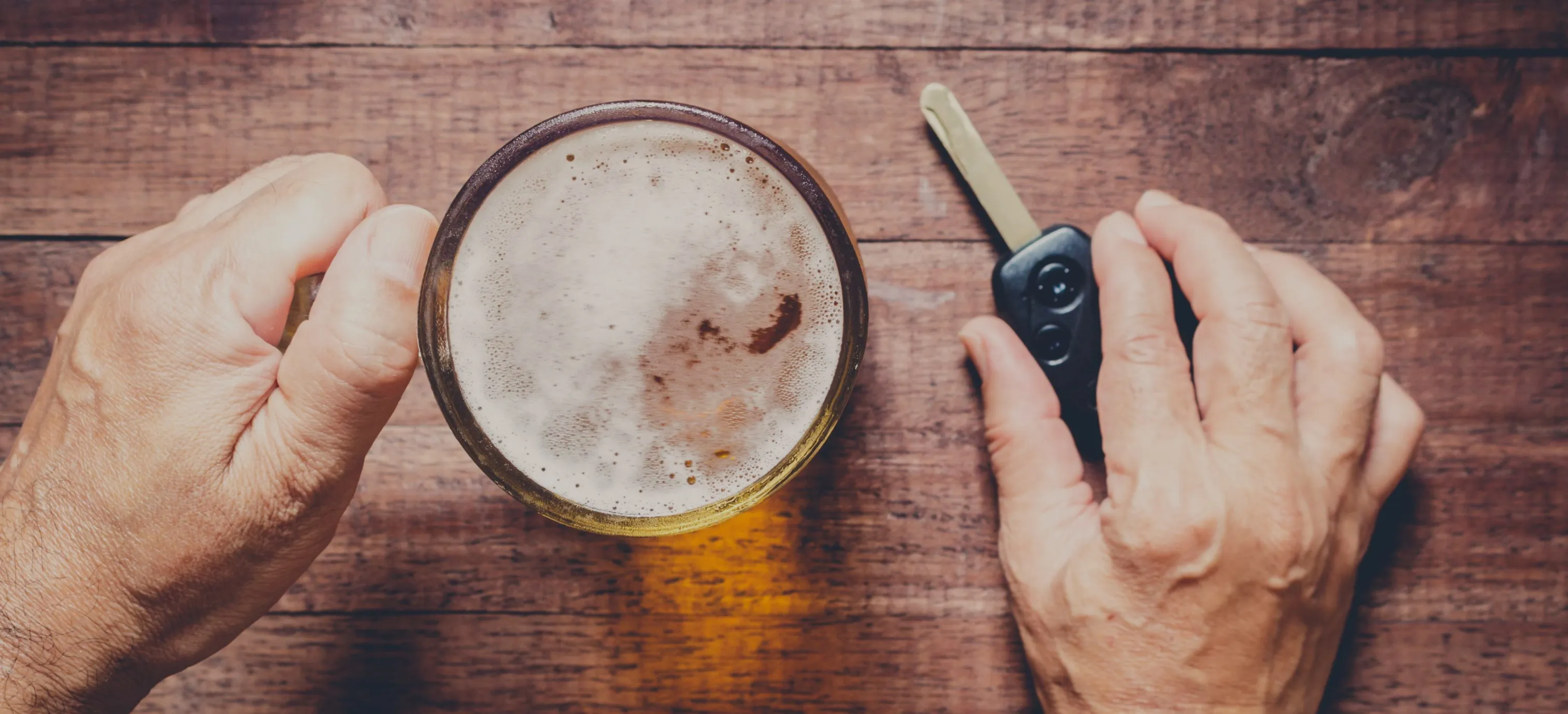 Top down view of a glass of beer in one hand and car keys in the other hand.