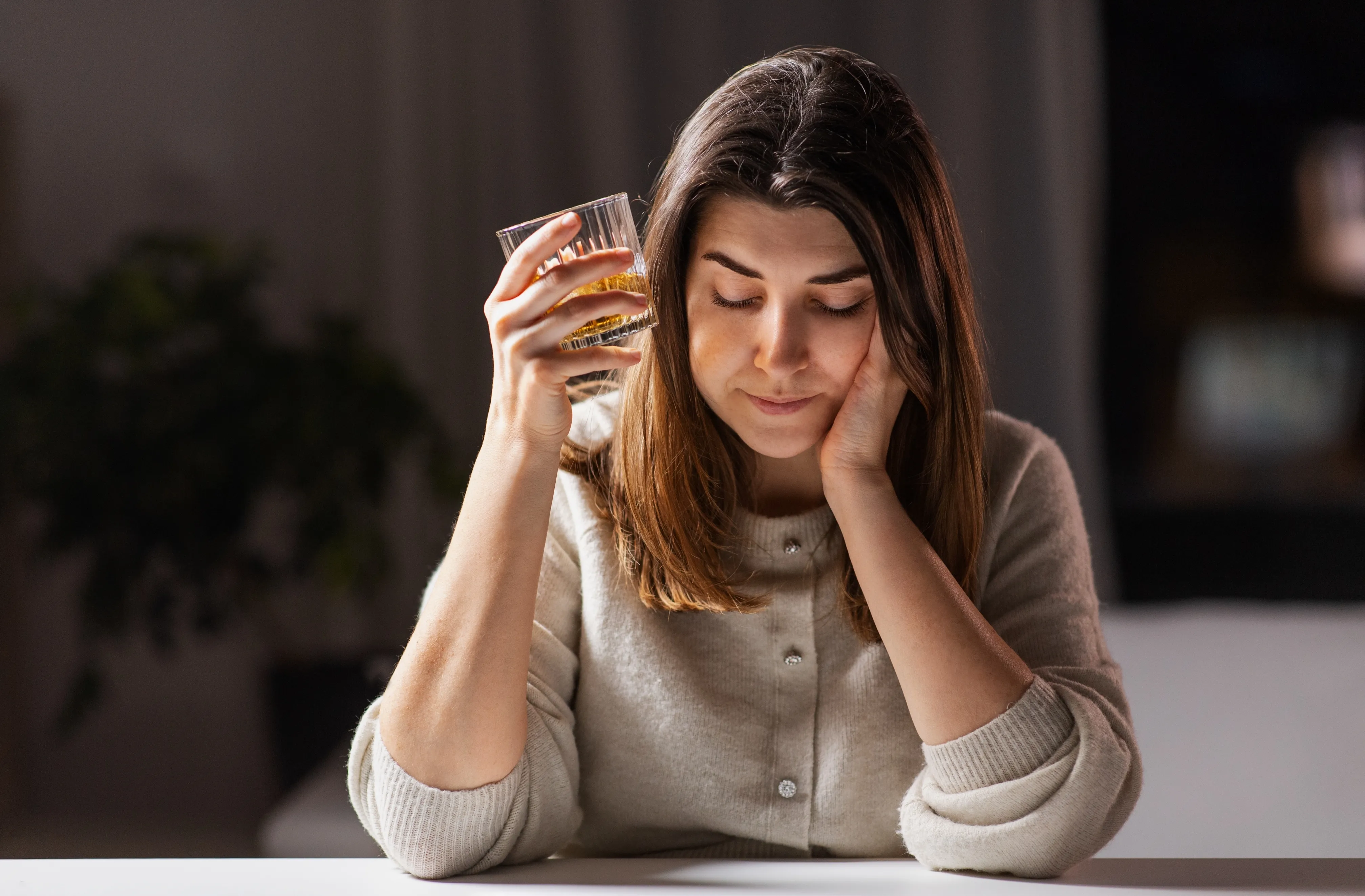 Woman holding alcoholic beverage in hand looking stressed and in need of support.