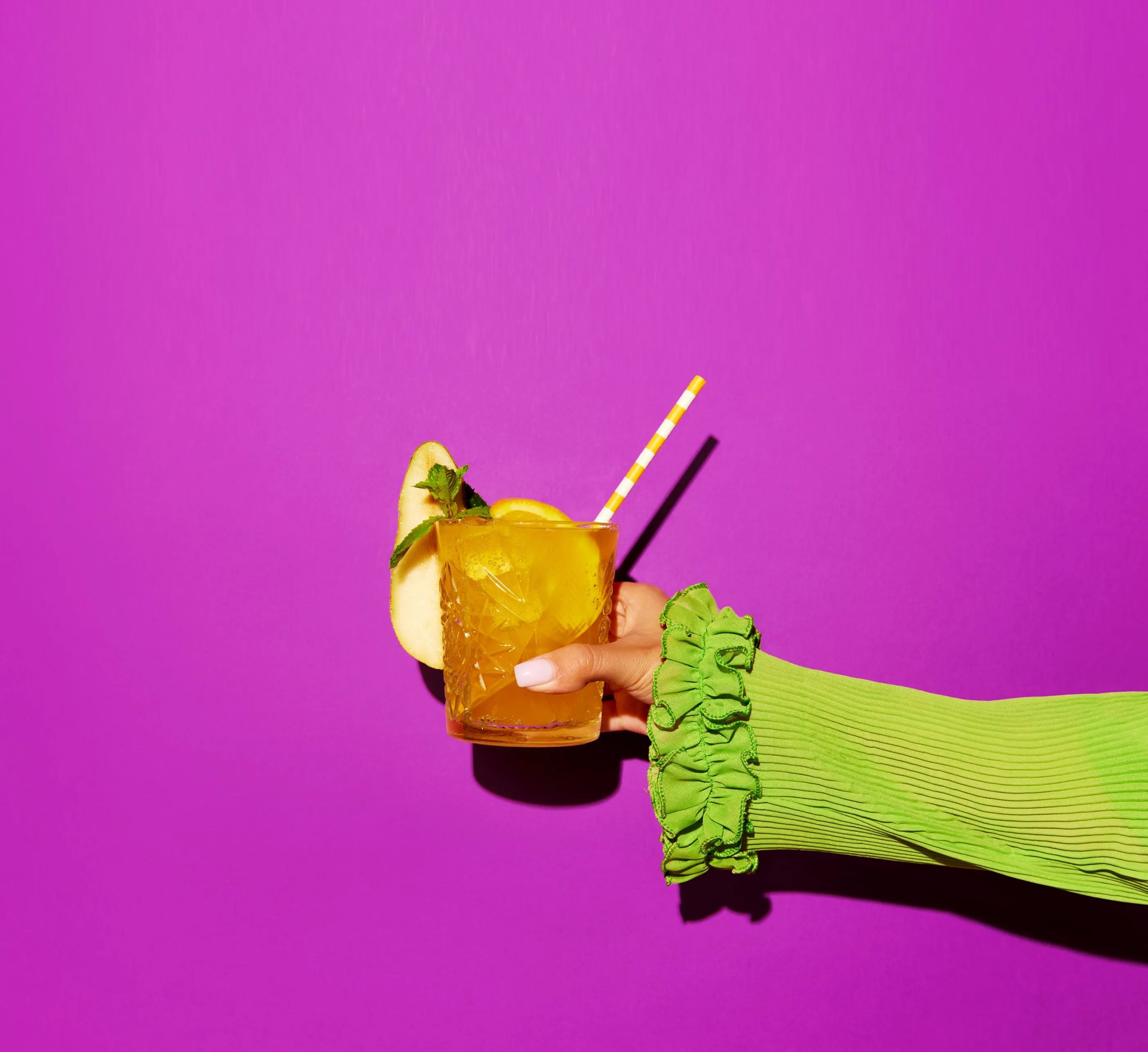 Hand holding glass of colorful non-alcoholic cocktail over bright pink background.