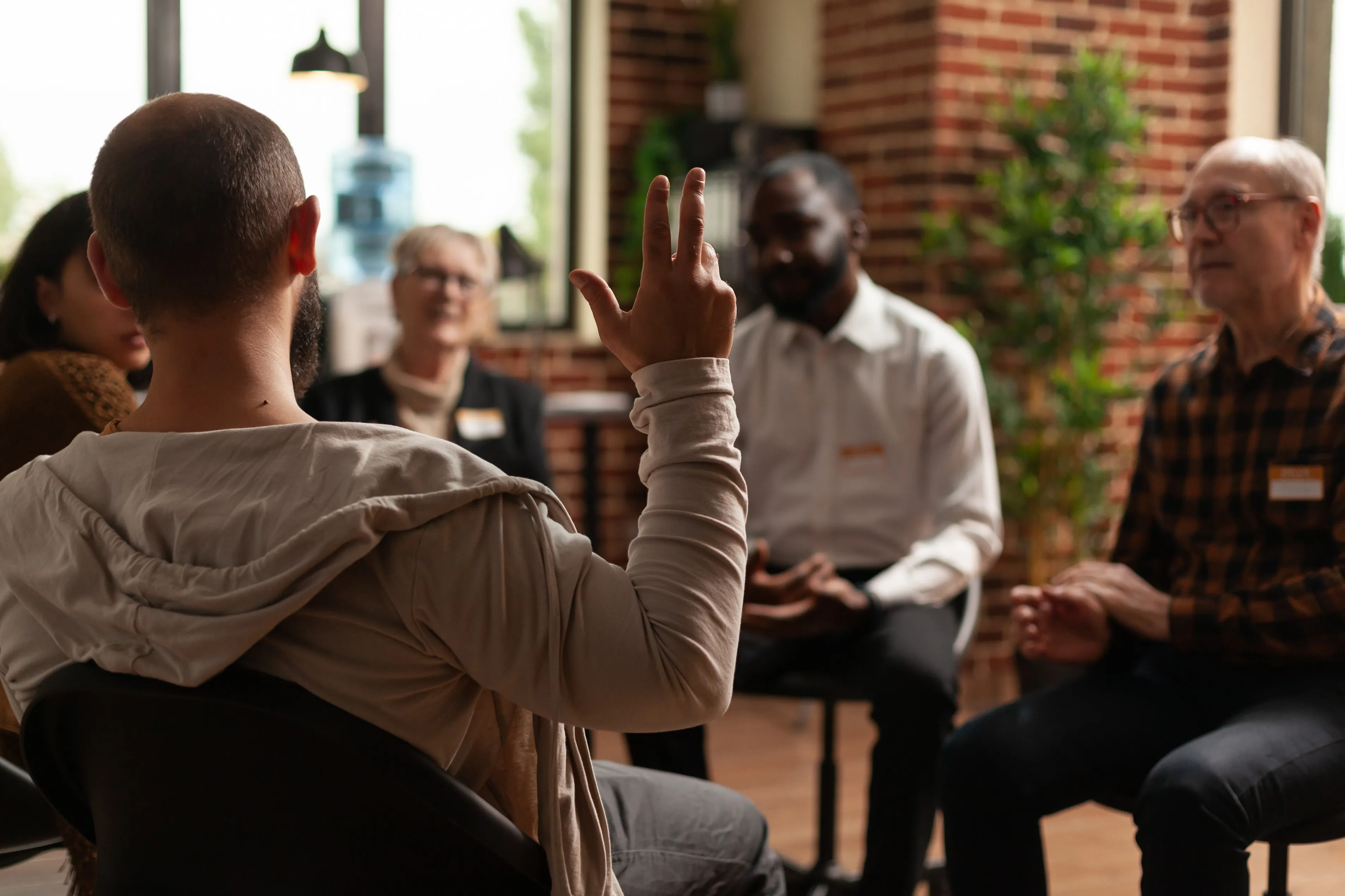A group of adults sitting in a circle with one man raising his hand to speak.